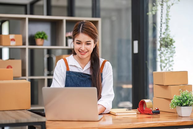 woman with work apron sitting at desk typing on a laptop